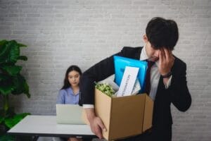 hombre de negocios con una caja de carton saliendo mientras la mujer de negocios trabaja en el fondo scaled 1